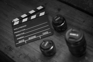 Monochrome image featuring a clapperboard and camera lenses on a wooden table.